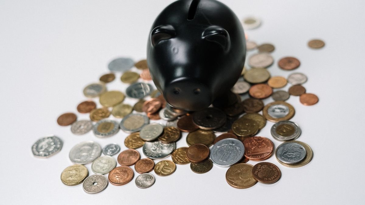 Hucha negra rodeada de monedas sobre una superficie blanca